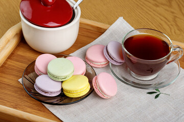 Multicolored macaroons and a cup of tea on a wooden tray. Morning tea and sweets.