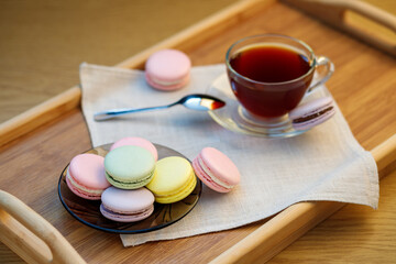 Multicolored macaroons and a cup of tea on a wooden tray. Morning tea and sweets.
