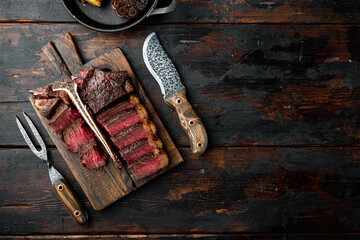 Porterhouse steak is grilled sliced on a piece, on wooden serving board, on old dark  wooden table background, top view flat lay, with copy space for text