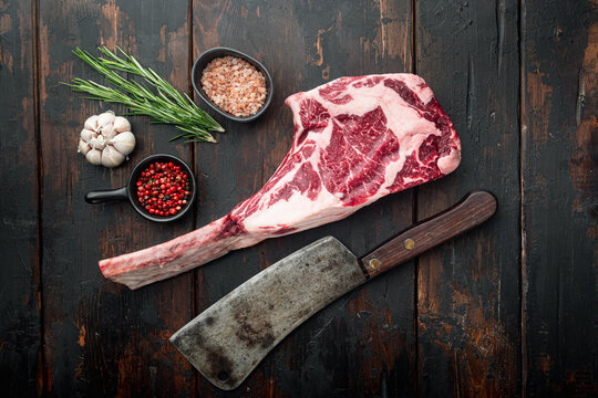 Raw uncooked black angus beef tomahawk steak on bone, and old butcher cleaver knife, with seasoning and herbs, on old dark  wooden table background, top view flat lay, with copy space for text