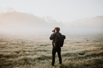 Fotograf auf einer nebligen Wiese macht Foto von der Landschaft