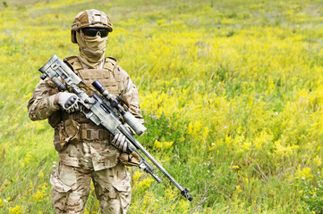 Equipped and armed special forces soldier in the blooming field with copy space for text