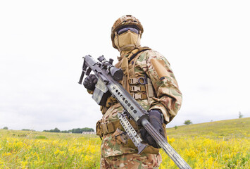 Armed special forces soldier with sniper rifle stands in field