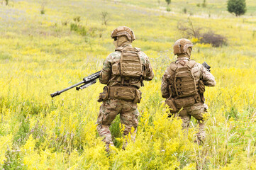 Two equipped and armed special forces soldiers with rifles in the blooming field