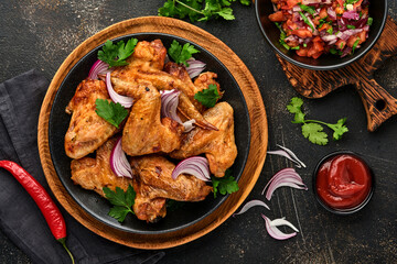 Grilled chicken wings or roasted bbq with spices and tomato salsa sauce on a black plate. Top view with copy space.