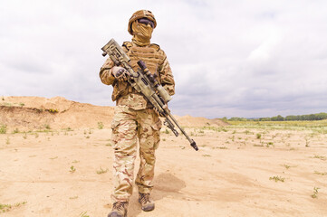 Equipped and armed special forces soldier with sniper rifle standing in the desert.