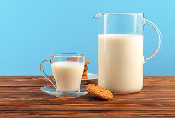 A jug and a glass of milk with cookies on a wooden table, on a blue background.Copy space.