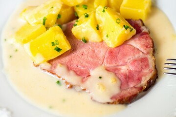 Smoked meat fillet with boiled potato and spicy horseradish sauce on white plate.