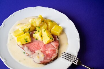 Smoked meat fillet, boiled potato and spicy horseradish sauce on white plate on blue.