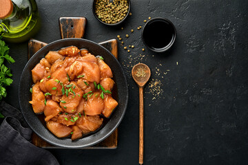 Raw chicken meat marinated in teriyaki soy sauce, onions and pepper in a black plate on a dark slate, stone or concrete background. Top view with copy space.