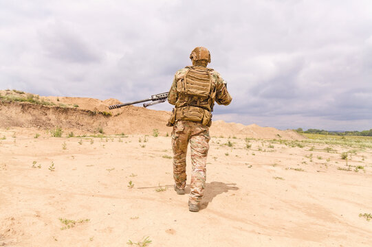 Special force soldier in camouflage with rifle walks across desert