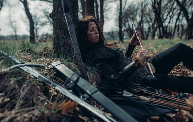 Fototapeta na wymiar Woman in image of medieval warrior lies and rests in forest.