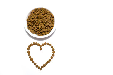 Dry food for cats and dogs in a white bowl. Heart from the food. Studio white background.