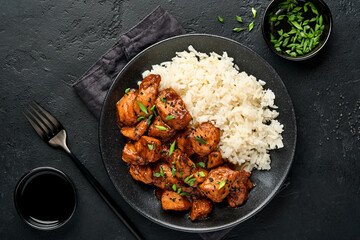 Spicy teriyaki chicken fillet pieces with rice, green onions and black sesame seeds on black plate...