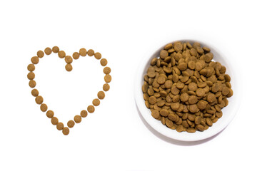 Dry food for cats and dogs in a white bowl. Heart from the food. Studio white background.