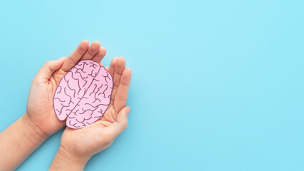 Woman hands holding human brain shape made from paper on light blue background. Awareness of...