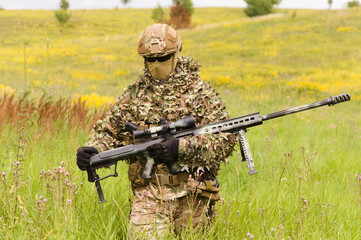 Special force soldier with sniper rifle walks across summer field