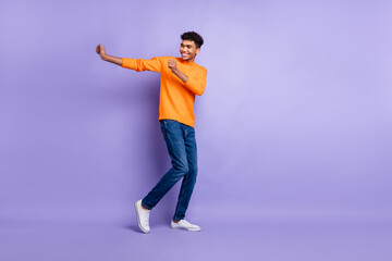 Photo of sweet funny dark skin guy dressed orange pullover dancing empty space isolated purple color background