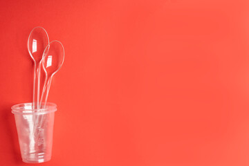 Transparent disposable cups and spoons on a red background. Drinking regime.Place for text