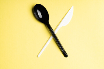 Black spoon and white knife crosswise on yellow background. Plastic cutlery, ecology, environmental pollution by plastic, disposable tableware, waste recycling concept. copyspace