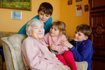 Great-grandmother with three children, siblings. Family of four, two boys and little toddler girl. Happy senior old woman and grandchildren, indoors.