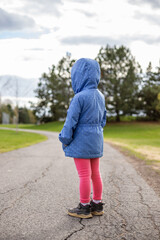 Little girl standing on a road in the park in spring. Child from behind.