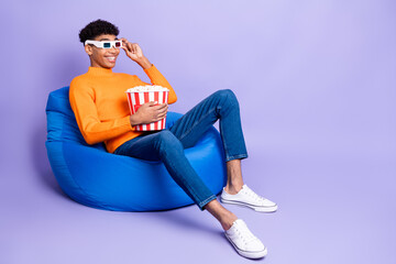 Photo of excited dark skin man wear sweater sitting beanbag eating popcorn watching movie isolated violet color background