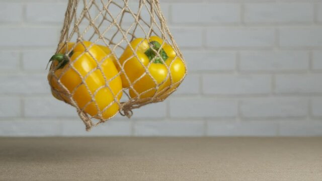 String bag with eco peppers. A somebody puts an eco mesh bag with yellow peppers on the table.