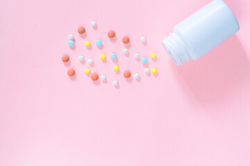 Multicolored tablets, pills, capsules in plastic bottle on pink background, copy space. Heap of assorted various medicine tablets and pills, vitamin and nutritional supplements concept.