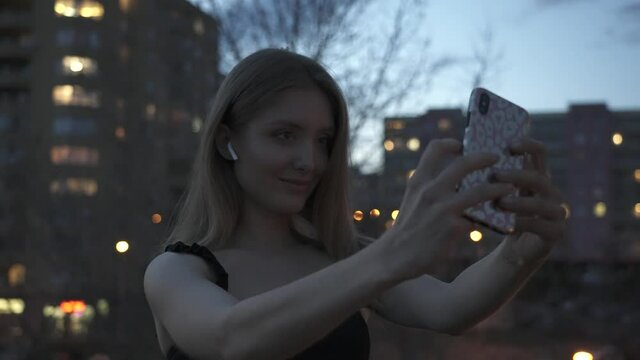 Young attractive woman taking selfie photo with smartphone in city twilight slow motion
