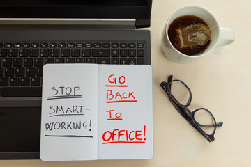 Laptop PC with glasses, cup with tea, and notebook with the words "stop smart working, go back to office". 
