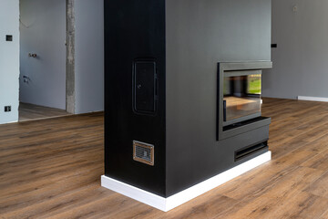 A modern fireplace with a closed combustion chamber standing in the living room, painted black,...