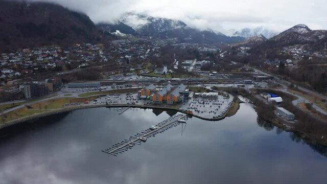 Arna city centre with railroad, parking, shopping centre and train station. Beautiful seawater reflections - ascending aerial tilt down from a distance