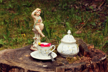 Vintage set consisting of angel, cup and sugar bowl on wooden stump, blurred background