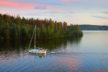 Sloop rigged yacht with inflatable boat sailing at sunset. Panoramic aerial view of the forest...
