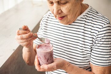 Beautiful old woman eating yogurt.