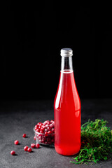 cranberry juice in a glass bottle on a black stone background, cranberry berries, green moss, vertical © Анастасия Коровина