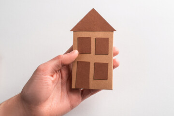 Close-up on a hand holding a paper house on white background
