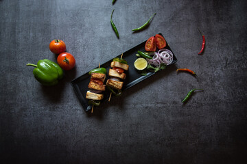 Top view of Paneer tikka in a tray. Paneer or cottage cheese tikka is an Indian dish made out of chunks paneer marinated with spices along with vegetables and grilled in a tandoor. 