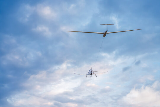 a motorized single engine plane towing a glider sailplane at takeoff into the clouds