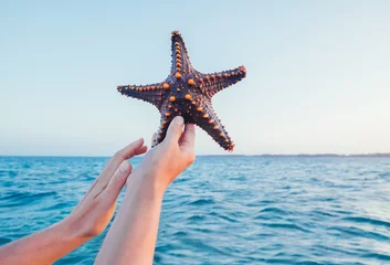 Fototapeten A Female's hands showing a starfish holding a live, large beautiful, and bright ocean inhabitant with sea waves background on Zanzibar island. Exotic vacation concept image. © Soloviova Liudmyla