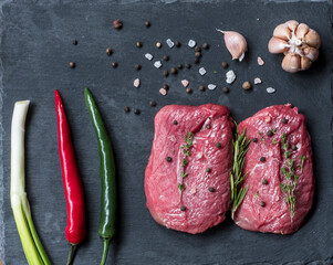 Two fresh raw beef steaks with spices, herbs on a black background