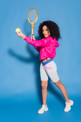 Fototapeta na wymiar full length of sporty african american woman holding tennis racket and ball while playing on blue
