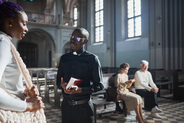 African priest talking to faithful woman after mass while they standing in the church