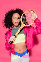 sporty brunette african american woman holding tennis racket on pink