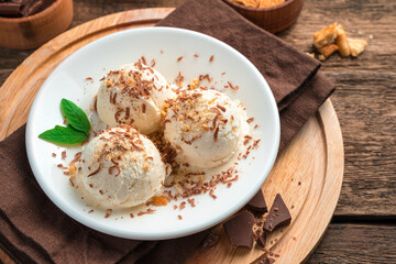 Three balls of creamy ice cream with chocolate chips and mint on a brown background.