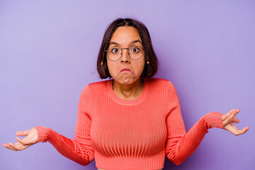 Young mixed race woman isolated on purple background shrugs shoulders and open eyes confused.