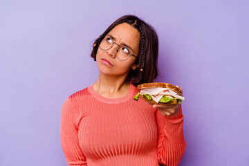 Naklejka premium Young mixed race woman holding a sandwich isolated on purple background dreaming of achieving goals and purposes