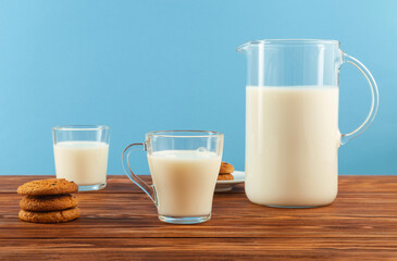 About the benefits of dairy products.A jug and a glass of milk with cookies on a wooden table, on a blue background.Copy space.