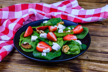Salad with spinach leaves, feta cheese, walnuts and strawberry on a black plate